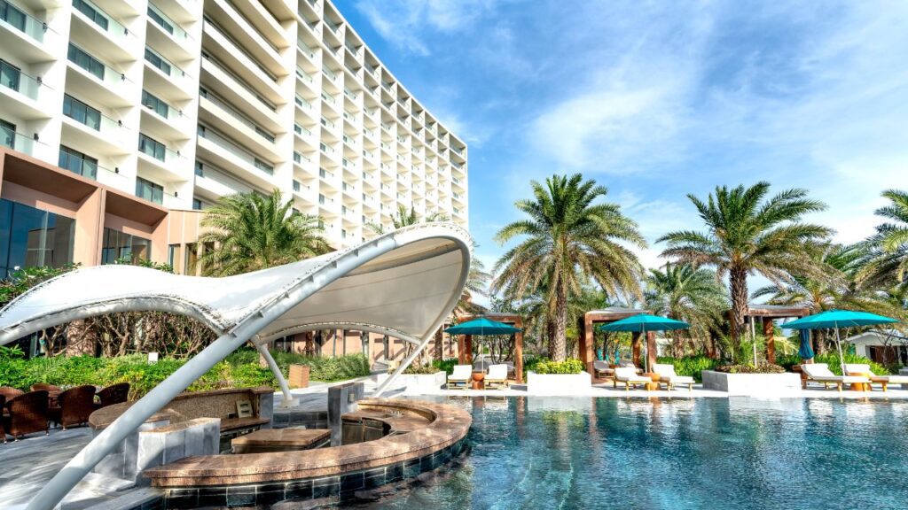 a luxury resort with pool and nearby relaxing couches and palm trees around