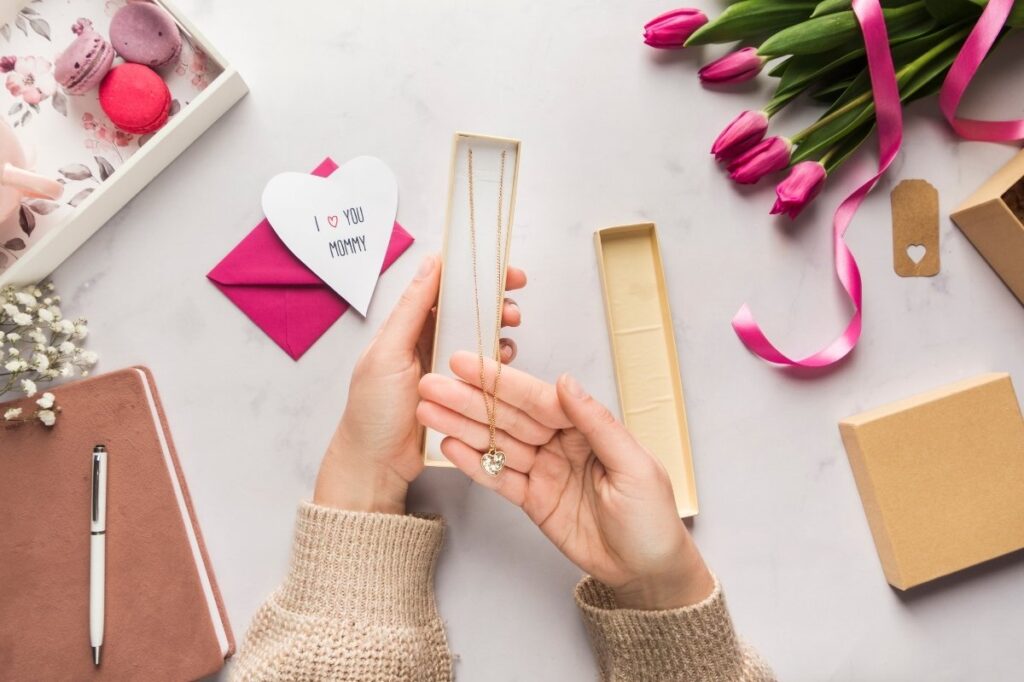 An image of a mom holding a personalised necklace with some gifts on table top
