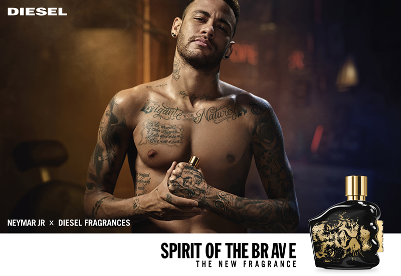 5 Football Stars Who Won the Fragrance Game 29 In this image Neymar Jr poses shirtless, showcasing his tattoos and confident demeanor in a dimly lit setting. Beside him is a sleek black and gold bottle of "Spirit of the Brave" by Diesel Fragrances, accompanied by the tagline "The New Fragrance.