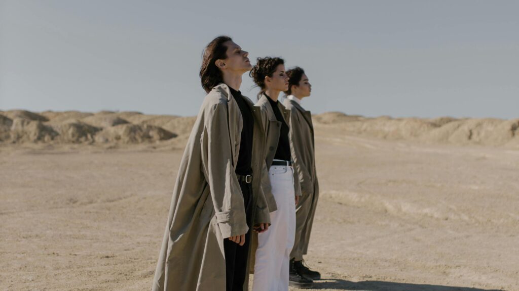 Three people in trench coats standing in a hot desert landscape