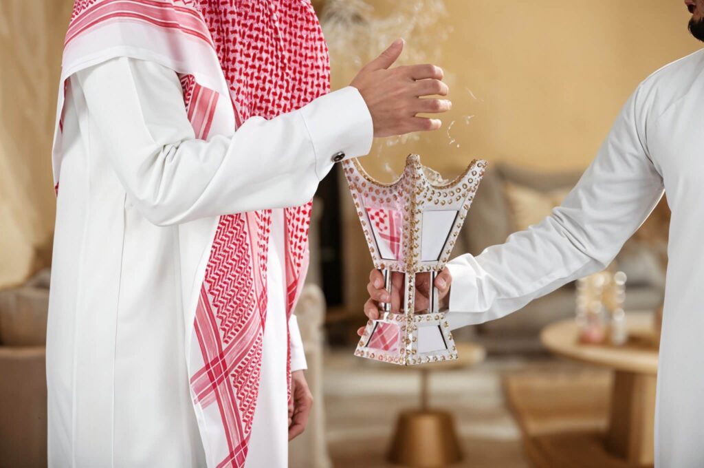 An image of 2 men in kandora with a bakhoor burner in one's hand.