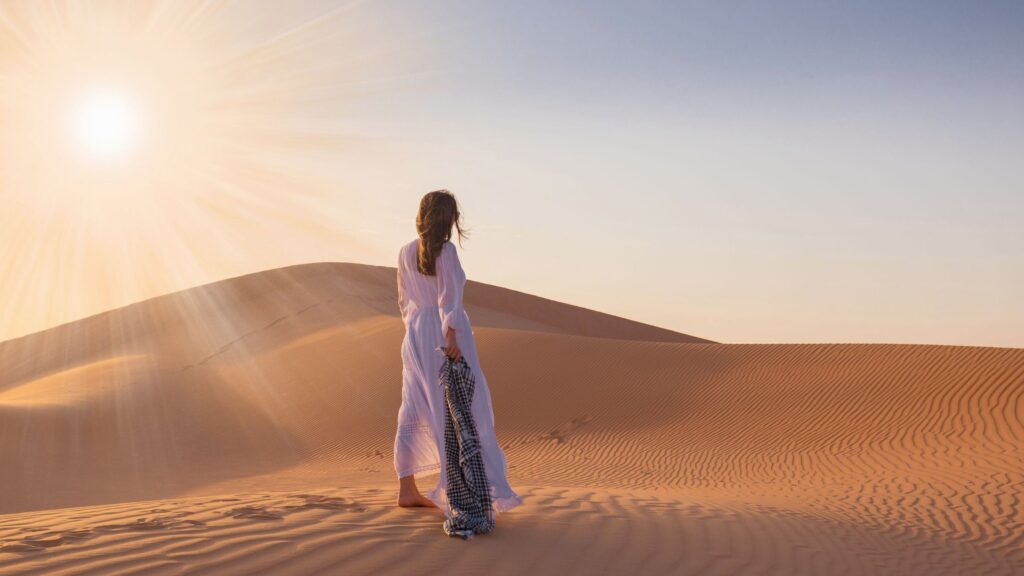 An image of a woman in the desert facing sun